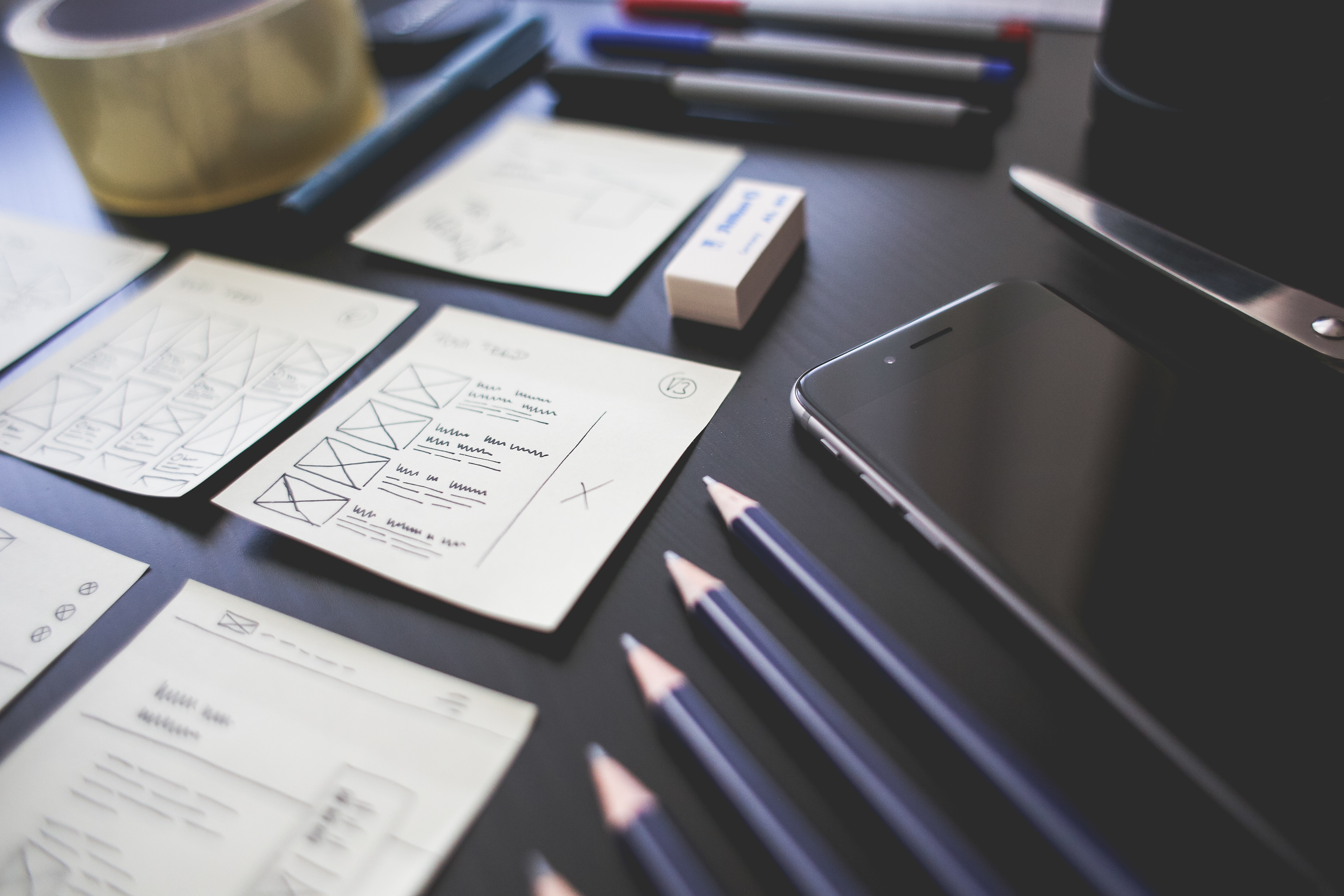 hand-drawn wireframes on a desk surrounded by various office supplies and a smartphone
