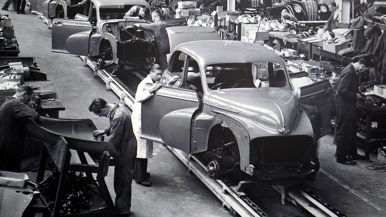 Black and white image of factory workers working in an assembly line building cars